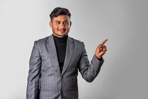 Portrait of a successful cheerful young man wearing formal suit pointing and presenting something with hand or finger with a happy smiling face. photo