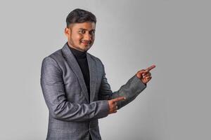 Portrait of a successful cheerful young man wearing formal suit pointing and presenting something with hand or finger with a happy smiling face. photo