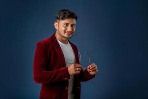 Portrait of Happy Indian young man wearing a blazer with eyeglasses posing on a blue background photo