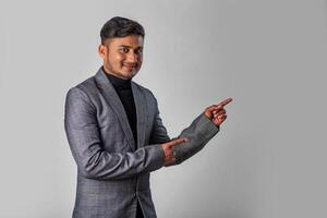 Portrait of a successful cheerful young man wearing formal suit pointing and presenting something with hand or finger with a happy smiling face. photo