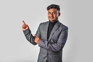 Portrait of a successful cheerful young man wearing formal suit pointing and presenting something with hand or finger with a happy smiling face. photo