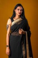 Portrait of a young beautiful girl wearing traditional black saree posing on a brown background. photo