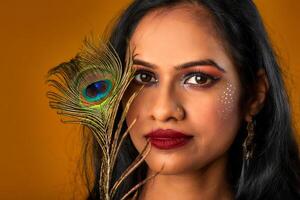 Beautiful Young Girl with bright makeup posing with peacock feathers on yellow background. photo