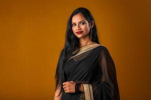 Portrait of a young beautiful girl wearing traditional black saree posing on a brown background. photo