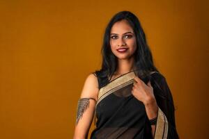 Portrait of a young beautiful girl wearing traditional black saree posing on a brown background. photo