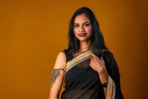 Portrait of a young beautiful girl wearing traditional black saree posing on a brown background. photo