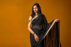 Portrait of a young beautiful girl wearing traditional black saree posing on a brown background. photo
