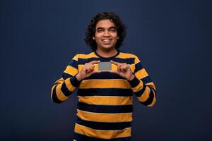 Young smiling handsome man posing with a credit or debit card on gray background. photo