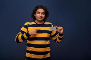 Young smiling handsome man posing with a credit or debit card on gray background. photo