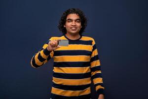 Young smiling handsome man posing with a credit or debit card on gray background. photo