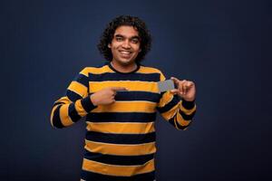 Young smiling handsome man posing with a credit or debit card on gray background. photo