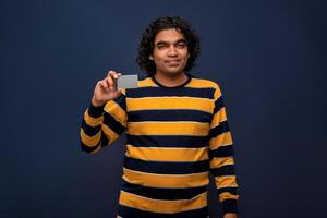 Young smiling handsome man posing with a credit or debit card on gray background. photo