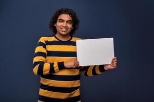 A happy young man holding and displaying a signboard or placard in his hands on a dark background. ready for your text or product. photo