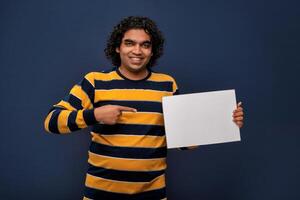 A happy young man holding and displaying a signboard or placard in his hands on a dark background. ready for your text or product. photo