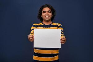 A happy young man holding and displaying a signboard or placard in his hands on a dark background. ready for your text or product. photo