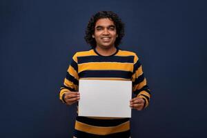 A happy young man holding and displaying a signboard or placard in his hands on a dark background. ready for your text or product. photo