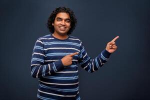 Portrait of a successful cheerful young man pointing and presenting something with hand or finger with a happy smiling face. photo
