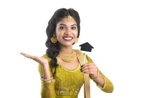 Happy Indian traditional young woman holding a little house cutout board in her hands on a white background. photo