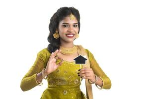 Happy Indian traditional young woman holding a little house cutout board in her hands on a white background. photo