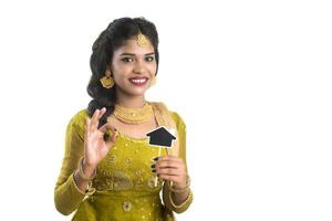Happy Indian traditional young woman holding a little house cutout board in her hands on a white background. photo