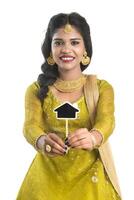 Happy Indian traditional young woman holding a little house cutout board in her hands on a white background. photo