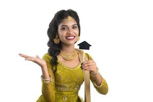 Happy Indian traditional young woman holding a little house cutout board in her hands on a white background. photo