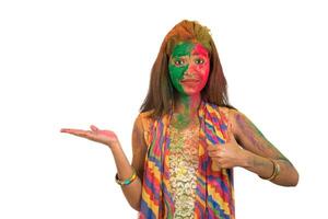Young girl with a colorful face holding and presenting something on the hand with a happy smiling on occasion of Holi festival. Festival and technology concept. photo