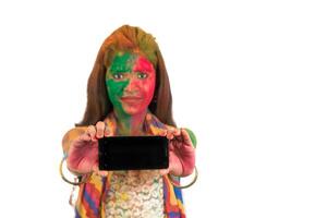 Young girl with colorful face showing smart phone screen on Holi festival. Festival and technology concept on white background. photo