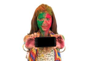 Young girl with colorful face showing smart phone screen on Holi festival. Festival and technology concept on white background. photo