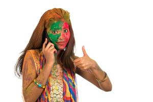 Young girl with colorful face talking on phone and celebrating festival of color Holi. photo