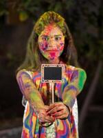 Young girl holding the small board on the occasion of Holi festival with faces painted with powdered colors, with a colour splash. photo