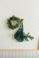 Christmas decor in the living room in the Scandinavian style, wreath of fir branches on the wall and a rag mesh bag string bag hanging on a hook photo