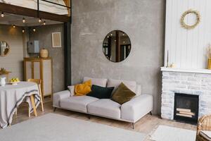 Gray sofa with pillows, a round mirror hangs on the wall in a modern Scandinavian-style living room near the fireplace and dining table photo