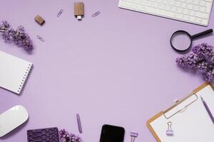 Minimal workspace on a home office desktop with notebooks, keyboard, stationery, coffee cup, bouquet of lilac flowers, smartphone. Flat lay, top view photo
