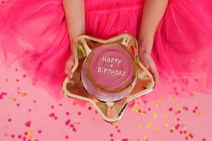 Girl in a pink dress holds in her hands a delicious sweet bento cake with the inscription happy birthday on a golden plate in the form of a star. Portioned trendy desert for one person photo