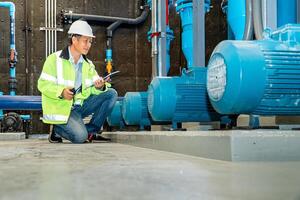 asian man worker in protective uniform and with hardhat using tablet for checking temperature in pipes Factory interior. photo