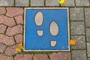 blue sign with two black feet on it is on a brick sidewalk. The sign is placed on a section of the sidewalk that is made of red and white bricks photo
