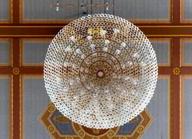 A large, crystal chandelier hangs from the ceiling of a room with an ornate pattern photo