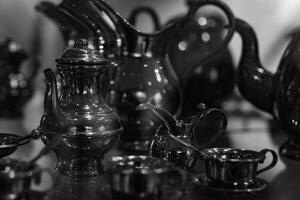 A collection of silver teapots and cups are displayed on a table photo