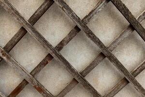 A close-up view of a weathered wooden trellis, showcasing its intricate diamond pattern against a textured background photo