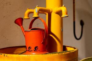 A red watering can sits on top of a yellow water pump with multiple spouts photo