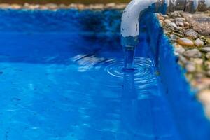 Water flows from a faucet into a blue basin, creating ripples in the still water photo