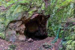 small cave is surrounded by moss and rocks. The cave is dark and damp, with a musty smell. The moss and rocks give the cave a sense of age and history. The cave is a natural wonder photo