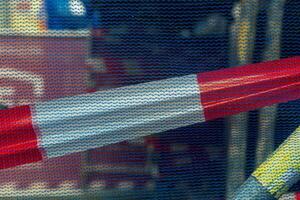 A red and white striped barrier is seen through a blue mesh fence, blocking access to a construction site photo