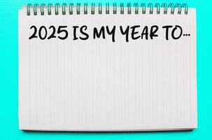 Words 2025 is my year to on white notebook. 2025 is my year to, word on notebook with green background. New year concept with typographic 2025 on paper. Motivational words for the new year 2025 photo