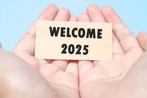 Hand holding a note Welcome 2025 with a blue background. New year concept with typographic 2025. Motivational words to welcome the new year 2025 photo