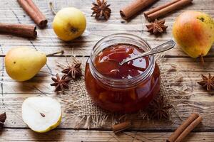 Homemade pear jam in a jar and fresh pears on a wooden background. photo