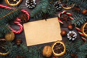 Frame of Christmas tree cones oranges caramel cane nuts on dark wooden background. Copy space. Flat lay. Old paper for text. photo