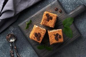 Pieces of tiramisu cake with delicate cream, coffee beans and mint leaves. Dark concrete background with copy space. Top view. photo