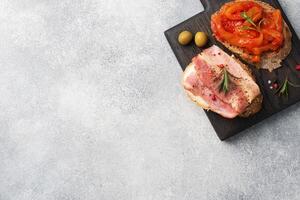 Whole grain bread sandwiches with cream cheese, bacon and canned peppers with tomato on a wooden cutting Board. Gray concrete background with Copy space. photo